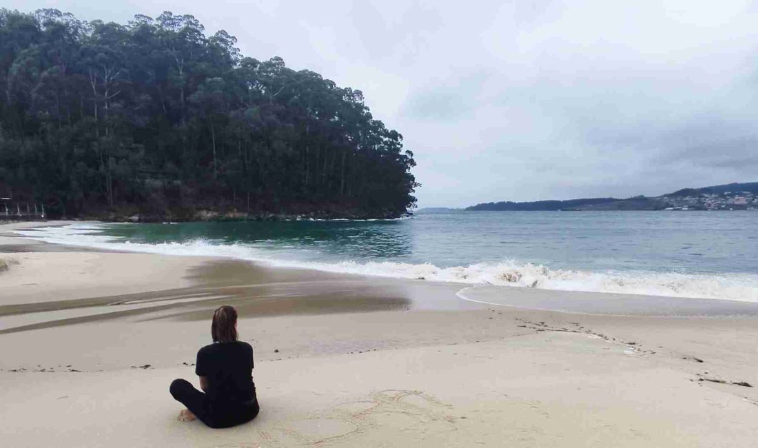 Mujer sentada en la playa reflexionando, símbolo de calma y equilibrio emocional en el coaching