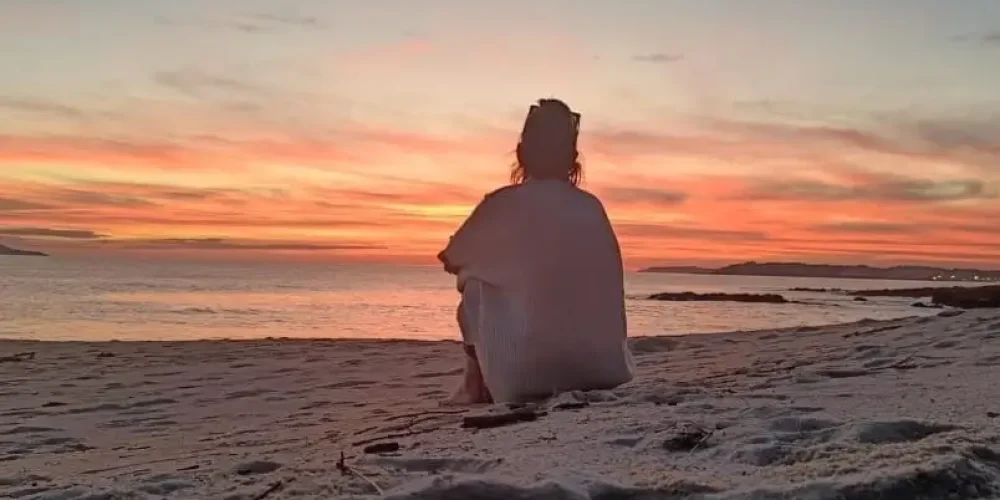 Ahogo emocional. Una persona sentada en la arena de la playa mirando al horizonte.