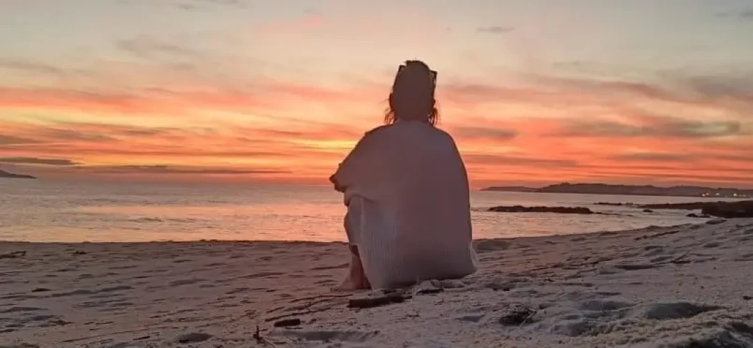 Ahogo emocional. Una persona sentada en la arena de la playa mirando al horizonte.